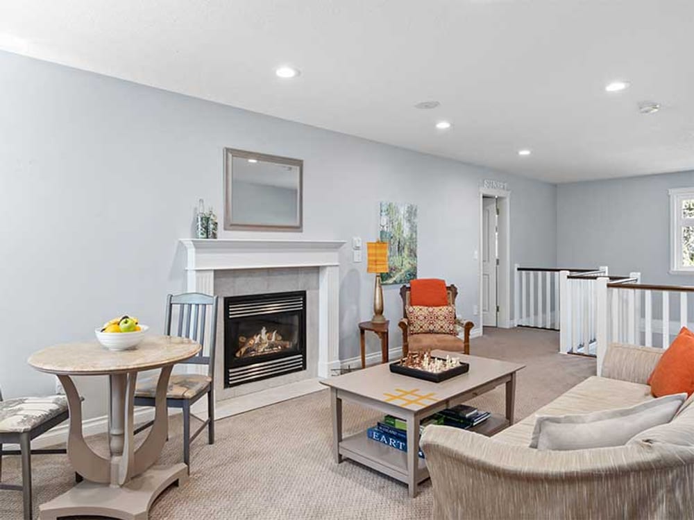 The guest lounge with a white fireplace, armchairs around a low table, and a bowl of fruit on the table by the window.