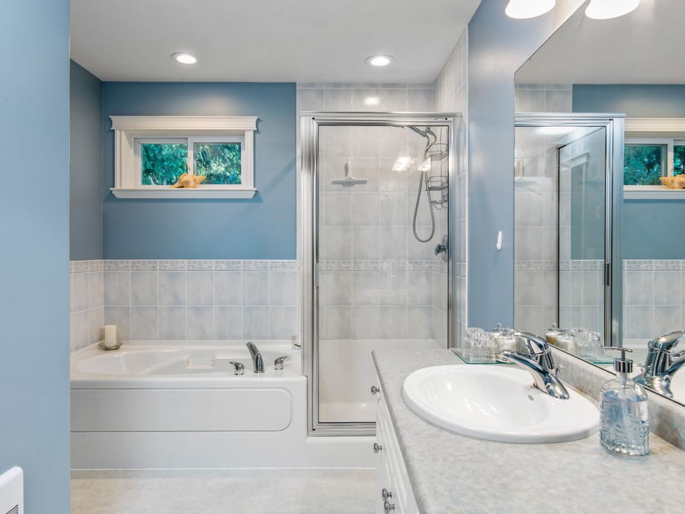 A bathroom with a soaker tub beside a glassed walk-in shower, and a wide vanity under the mirror.