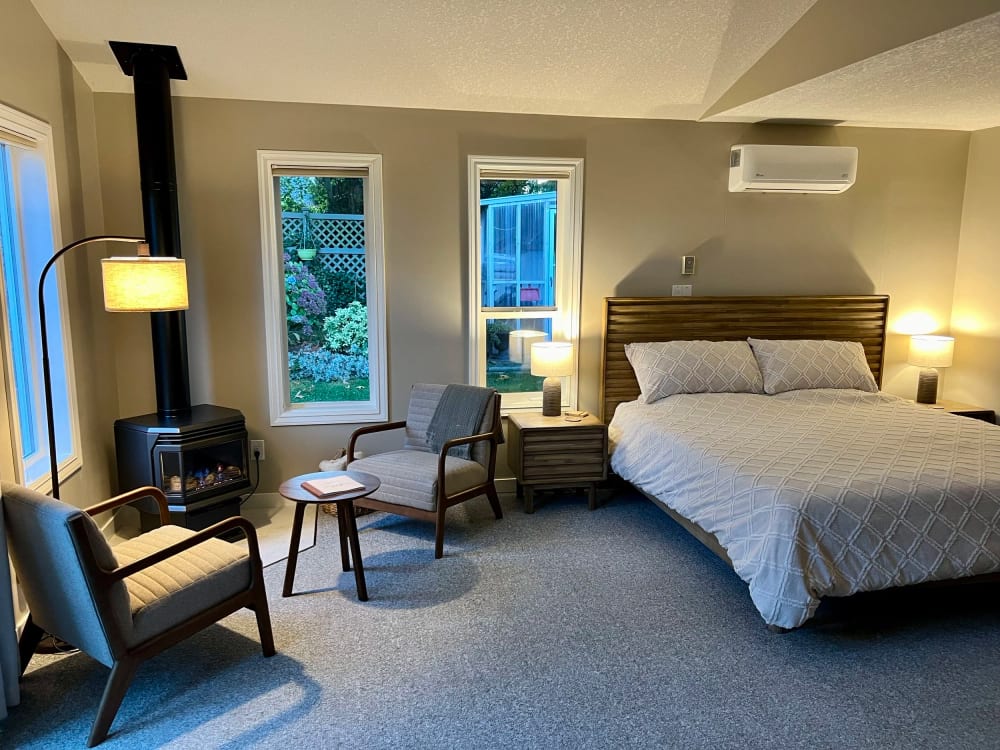 The garden suite: a king bed by the windows, a black gas fire and two armchairs, the garden beyond.
