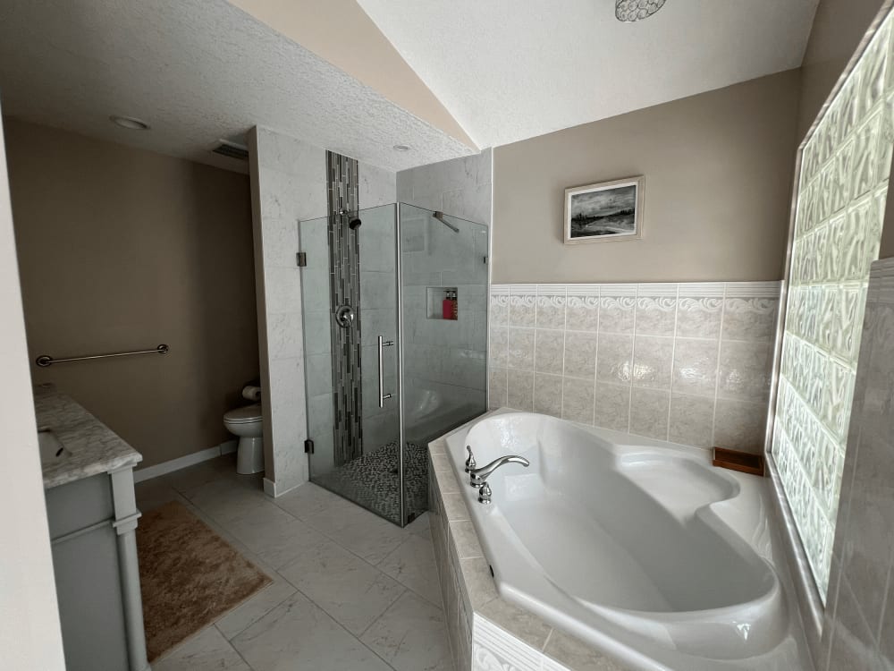An open five-piece bathroom with a glass walk-in shower, a soaker tub and a wide tiled vanity.