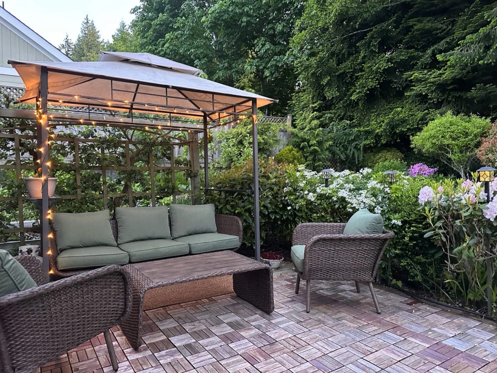 A brick patio under a timber pergola strung with lights, a cushioned sofa and chairs among the planting.
