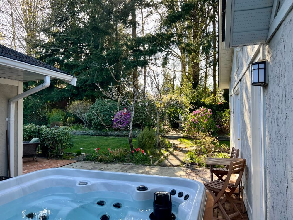 A mature garden of evergreens and shrubs, a lantern by the door and the hot tub set into the far corner.
