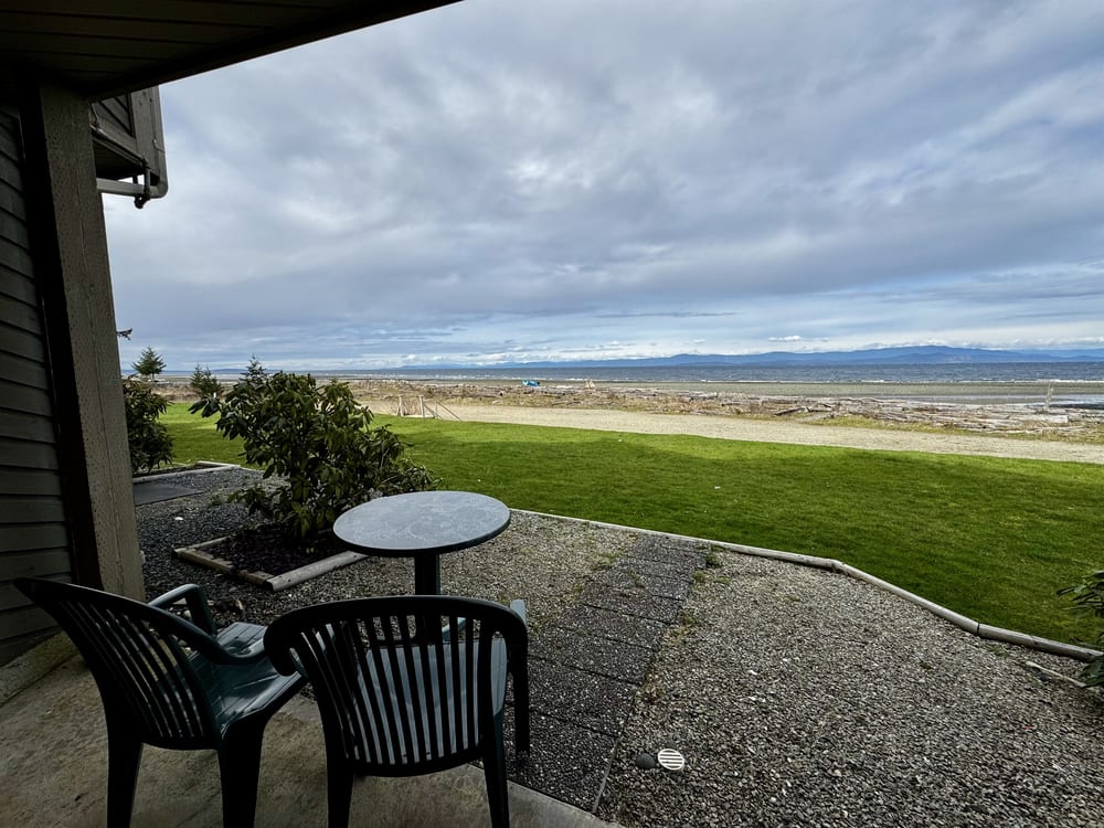 A private patio with seating, opening onto lawn and the beach beyond.