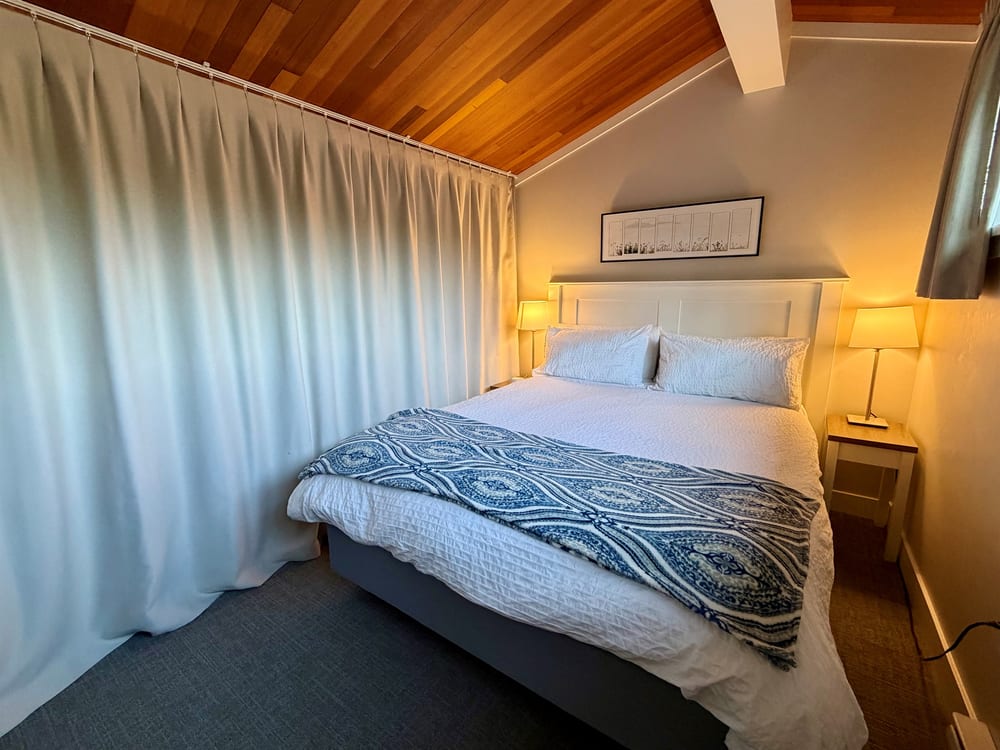 The upstairs sleeping loft with a queen bed and blackout curtains drawn back from the window.
